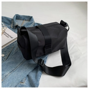 Detail of black nylon crossbody pillow bag with wide adjustable strap on denim jacket