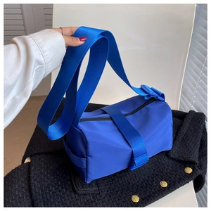 Detail of bright blue nylon barrel bag with wide shoulder strap on tweed background