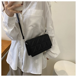 Detail of a black quilted shoulder bag with triangular stitching worn on a white shirt