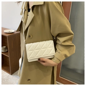 Quilted beige crossbody bag styled with a trench coat in a cozy indoor setting