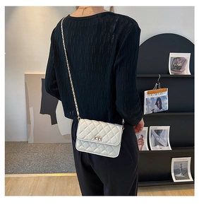 Close-up of a white quilted crossbody bag with a gold chain strap on a model