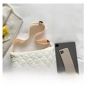 Detailed view of white quilted crossbody bag with wide strap next to a tablet for size scale