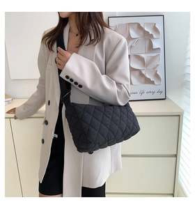 Detail of black quilted crossbody bag with adjustable strap worn by model in white suit