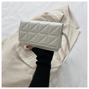 Close-up of white quilted leather crossbody bag with triangular stitching and long strap