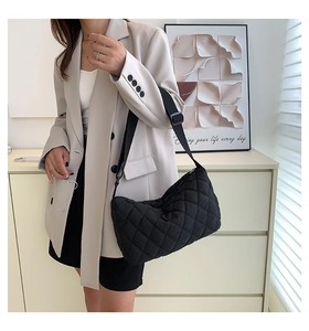 Close-up of black quilted crossbody bag with adjustable wide strap worn by a model