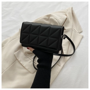 Close-up of black quilted crossbody bag with triangular stitching and leather shoulder strap