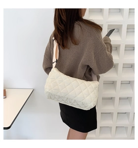 Close-up of beige quilted crossbody bag with diamond stitching on a female model