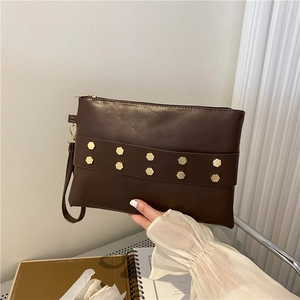 Brown faux leather envelope clutch bag with golden rivets and wrist strap held by hand