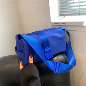 Blue nylon crossbody cylinder pillow bag with adjustable wide fabric strap and plastic buckle