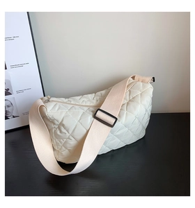 Detail of off-white quilted crescent moon bag with adjustable strap on a dark surface