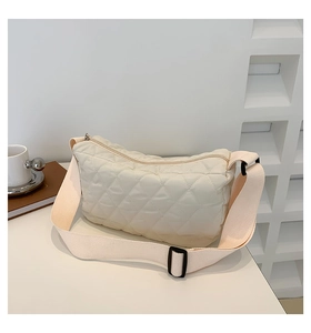 Close-up of cream quilted crossbody bag with wide shoulder strap and lattice shadow background