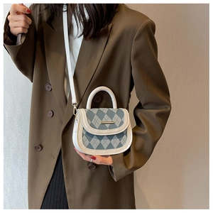 Detail of blue argyle quilted saddle bag with white trim worn by a model in a brown suit