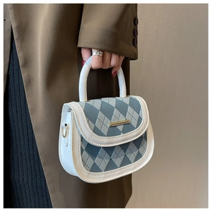 Close-up of diamond pattern blue gray handbag with gold metal bar and white trim details