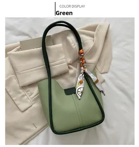 Détail du sac hobo vert avec bordure foncée et foulard en soie sur un drap blanc