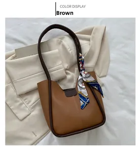 Détail d'un sac seau en cuir marron avec un foulard en soie imprimé entouré sur l'anse