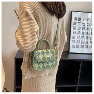 Detail of green quilted saddle bag with gold metal trim worn by model in home setting