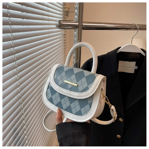 Detail of blue and white quilted saddle bag featuring a gold metal bar and leather handle