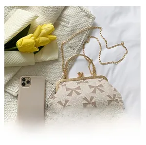 Detail of cream crossbody bag with textured bow pattern and gold metal frame closure