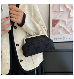 Close-up of black bow jacquard handbag with gold frame worn by model in white tweed jacket