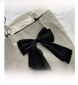 Détail du tissu blanc plissé avec un grand nœud noir et une bandoulière en chaîne argent