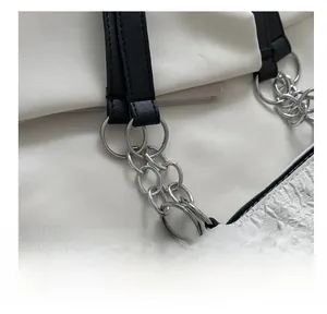 Détail de la bandoulière en PU noir et de la chaîne en métal argenté sur un sac blanc