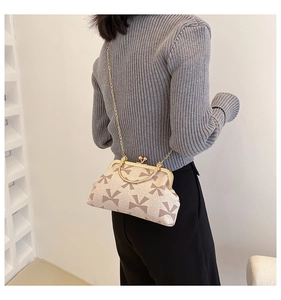 Detail of a vintage beige crossbody bag with bow patterns and a metal chain strap