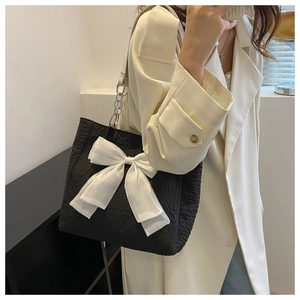 Détail du sac cabas noir texturé avec un grand nœud en satin blanc et chaîne en métal