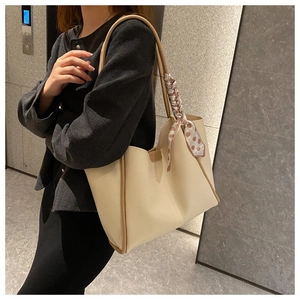 Close-up of beige tote bag with light brown leather trim and a brown polka dot scarf