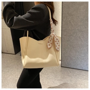 Detail of cream tote bag with wavy edge and brown polka dot silk scarf on the handle