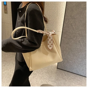 Detailed view of creamy tote bag with decorative polka dot scarf on a model