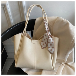 Detailed view of beige faux leather tote bag with elegant polka dot silk scarf on a chair