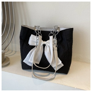 Détail d'un sac cabas noir avec une texture plissée et un grand nœud en soie blanche élégant