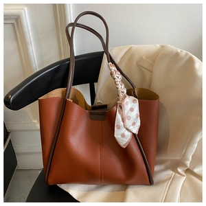 Brown leather tote bag with a polka dot silk scarf handle detail on a chair