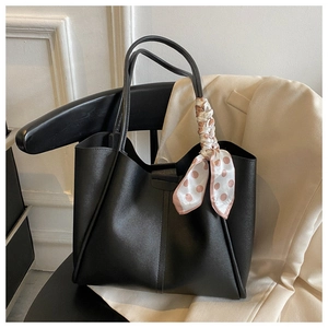 Detail of a large black faux leather tote bag with a pink polka dot silk scarf handle