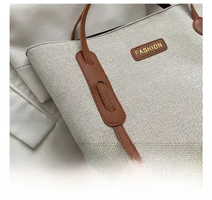 Close-up of beige canvas tote bag showing precise stitching and brown leather strap details