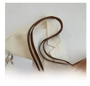 Detail of brown leather tote handle with white stitching against minimalist props
