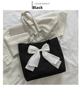 Détail d'un sac cabas noir avec nœud en organza blanc et bandoulière en chaîne argentée
