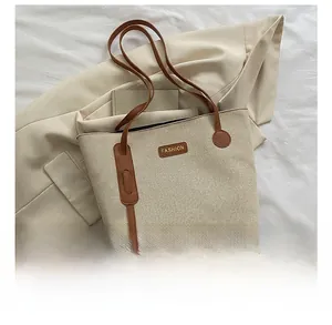 Detail view of beige canvas tote bag with brown leather handles and fashion logo