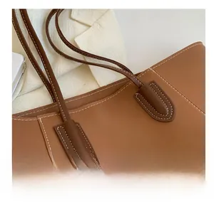 Detailed close-up of dark brown leather tote bag handle with contrast stitching