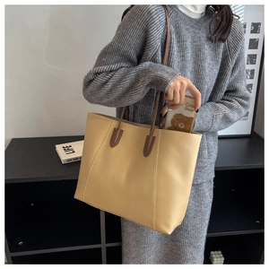 Detail of a large beige tote bag with coffee brown straps worn by a model in casual attire