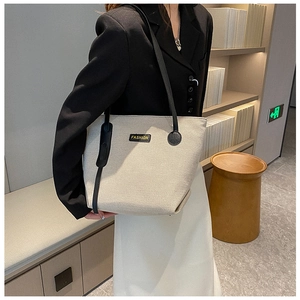 Detailed side view of a large beige canvas tote bag with black straps and fashion label