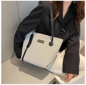 Detail of a large canvas tote bag with black leather straps worn by a model in a minimalist setting
