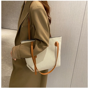 Detail shot of canvas tote bag with brown leather straps worn over a classic trench coat