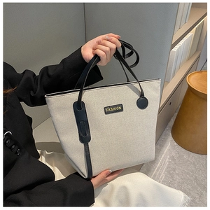 Detail of beige canvas tote bag featuring black leather handles and fashion logo patch