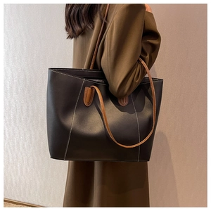 Detail of black tote bag with brown contrast stitching and long handles on a model