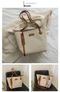 Detail of canvas tote bag showing beige fabric, brown leather handles, and fashion lettering