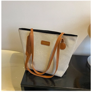 Detail view of large canvas tote bag featuring brown leather handles and fashion logo label