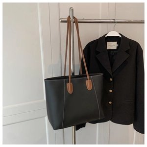 Detail view of large tote bag with black faux leather and brown handles with white stitching