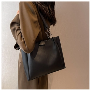 Detail of black faux leather tote bag with silver chain buckle on a model shoulder