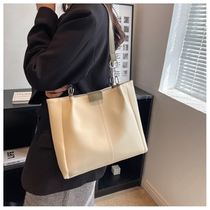 Detail of a large beige tote bag with vertical quilting and chain-link shoulder straps